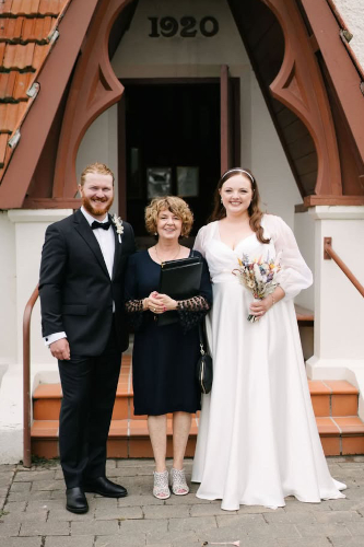 Bride, groom and celebrant posing in front of an old church.
